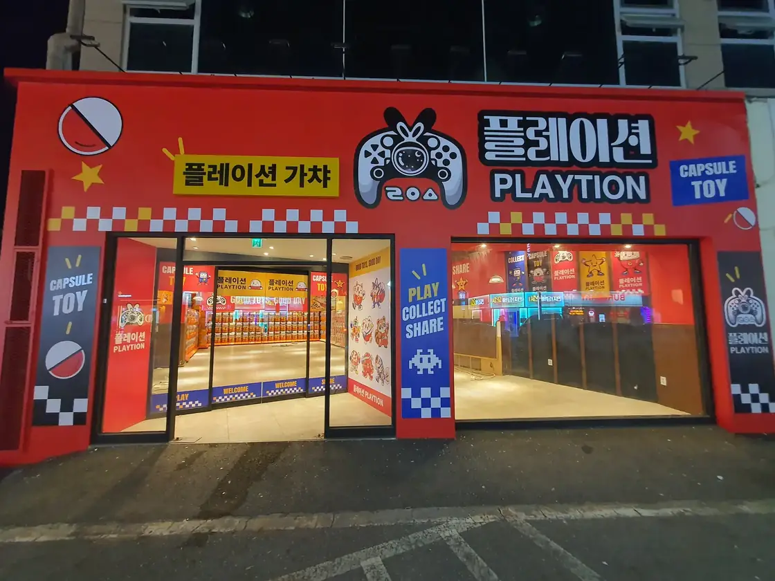 빨간 외벽에 노란 간판이 달린 플레이션 가챠샵 입구