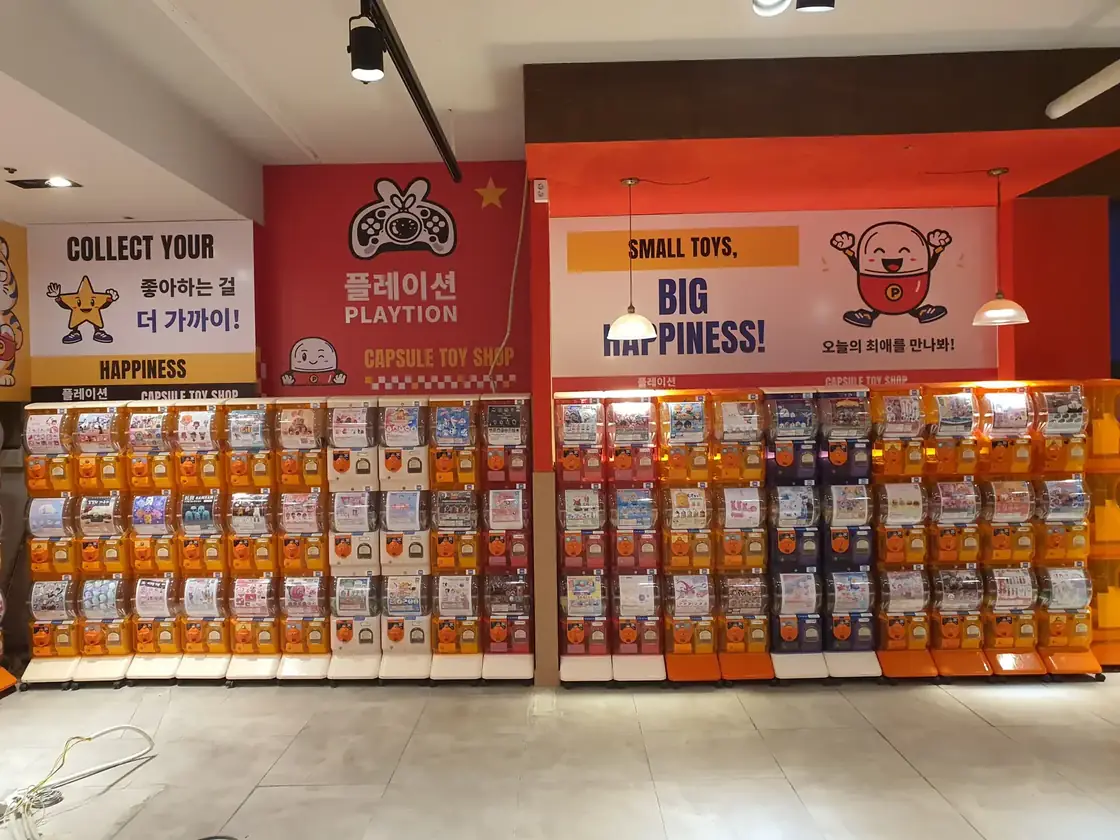 주황색 캡슐토이 기기가 벽면을 따라 늘어선 가챠샵 내부